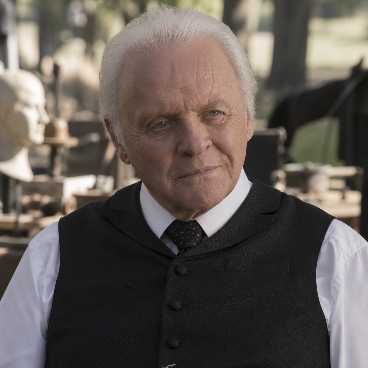Anthony Hopkins as Dr Robert Ford, wearing a black waistcoat and tie beside a Western town.