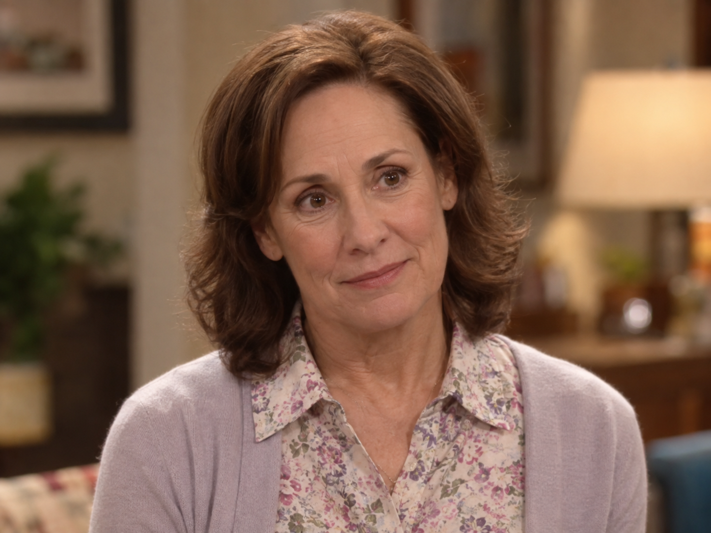 Laurie Metcalf as Mary Cooper, with softly waved brown hair and a pale lavender cardigan over a floral blouse, against a softly blurred interior.