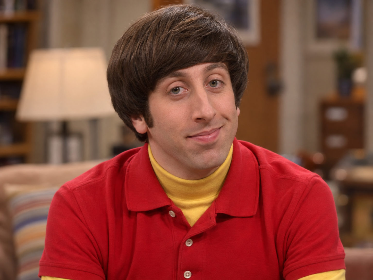 Simon Helberg as Howard Wolowitz, with a brown bowl haircut and a red polo shirt over a yellow top, against a softly blurred interior.