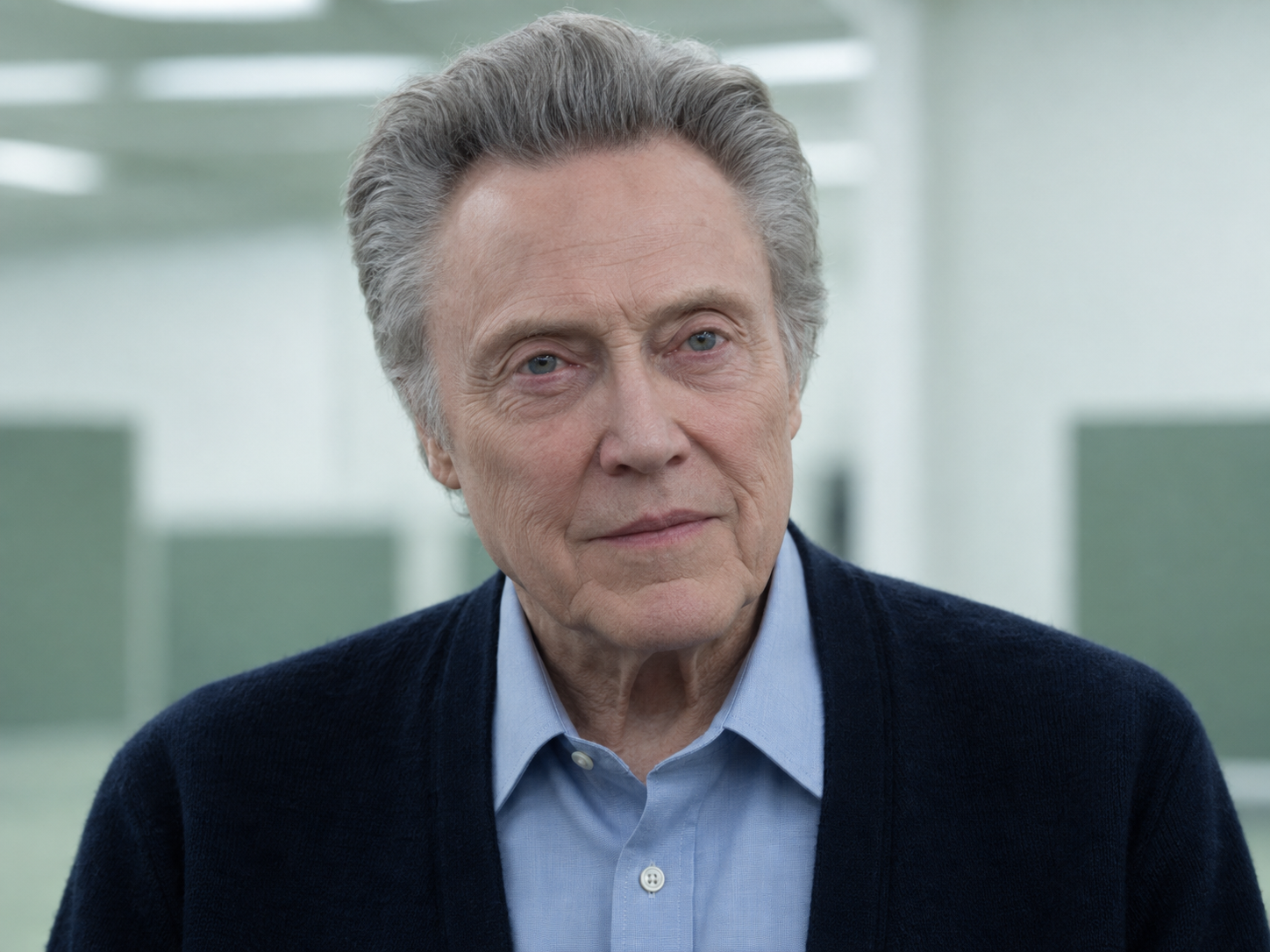 Christopher Walken as Burt in Severance, wearing a navy cardigan over a blue shirt against a softly blurred pale office.